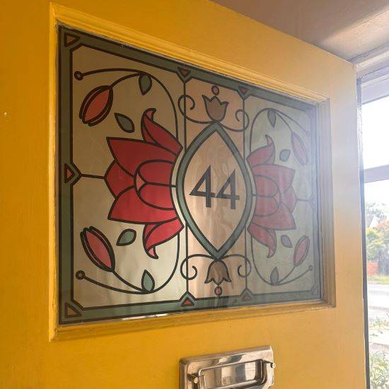 Lee stained glass window film with red lotus flowers and a center door number installed in a yellow door.