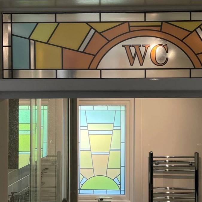A sun stained glass window film with the text WC installed above a bathroom door