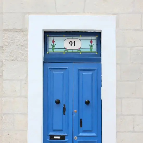 A simple flower stained glass window film design with a central house number installed onto a blue front door.