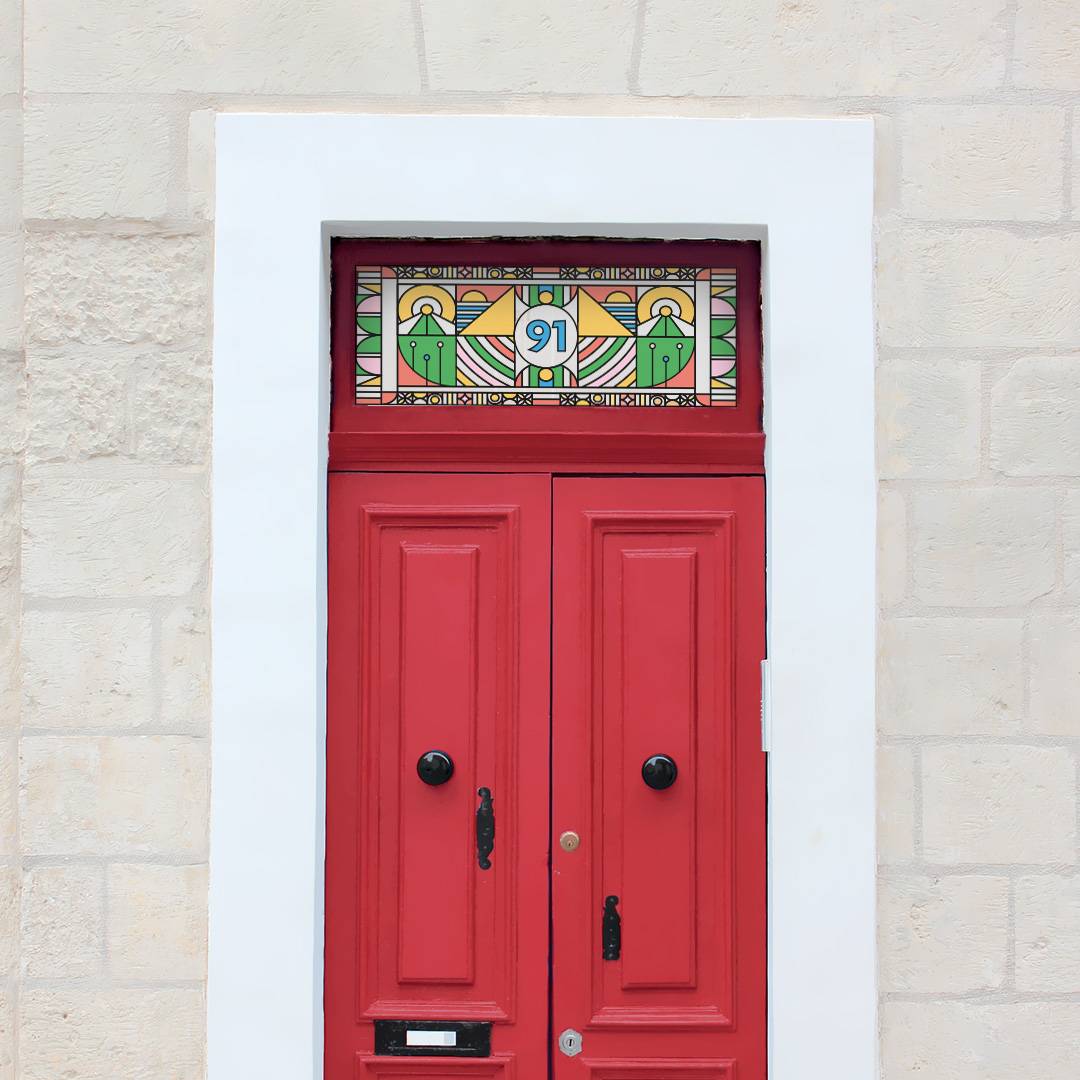 a bright and colourful modern stained glass window film with a central door number installed above a red door