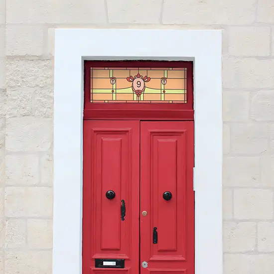 Nancy stained glass window film in an orange, yellow and red colour and a center house number installed above a red door.