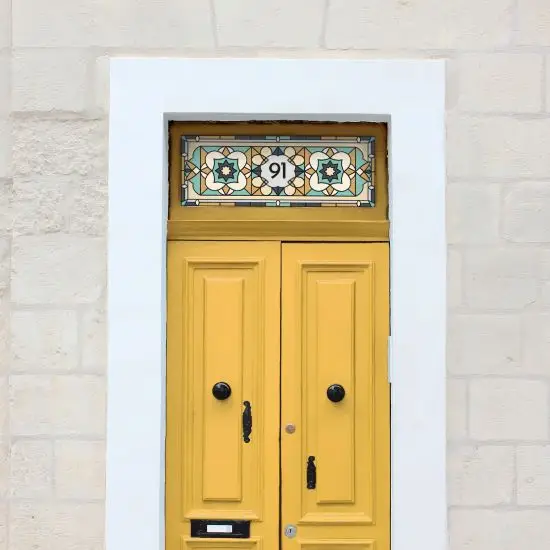 A cream and pastel stained glass window film installed above a yellow front door with a center house number.